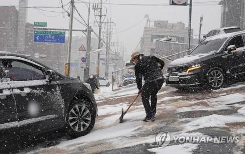 A person sweeps away snow on a road in western Seoul on Dec. 18, 2021, after the capital experienced the season's first heavy snow.