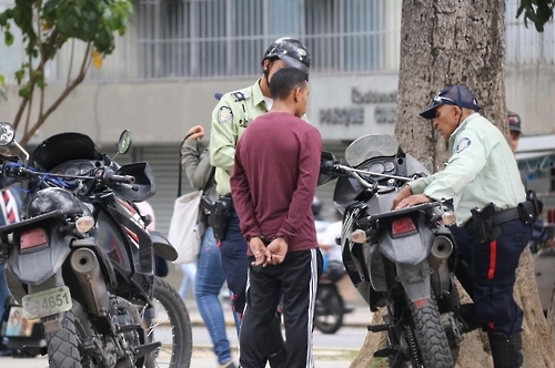 카라카스 시내에서 스마트폰을 훔치다가 경찰에 잡힌 현행범이 수갑을 차고 서 있다.