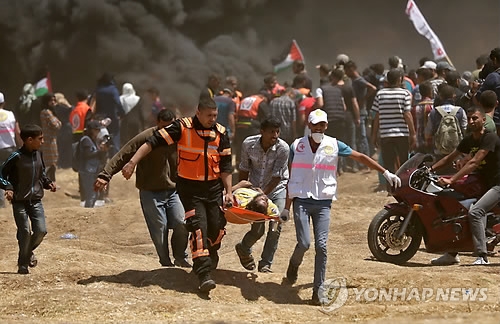 이스라엘 주재 미국대사관이 예루살렘으로 이전한 14일(현지시간) 팔레스타인 가자지구의 이스라엘과의 접경에서 대규모 항의시위가 벌어진 가운데, 팔레스타인 구호대원들이 이스라엘 군과의 충돌로 부상한 주민을 들것에 실어 옮기고 있다.[AFP=연합뉴스]