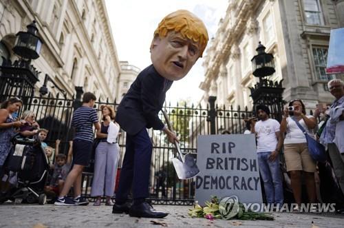 (런던 EPA=연합뉴스) 보리슨 존슨 총리의 가면을 쓴 시위자가 28일(현지시간) 영국 런던 다우닝가 10번지 총리관저 앞에서 총리의 의회 정회 결정에 항의하는 퍼포먼스를 하고 있다.