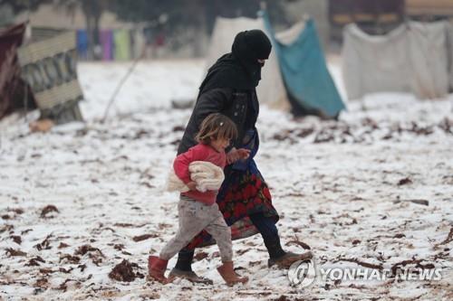 눈 내린 시리아 북서부의 피란민 캠프에서 이동하는 여성과 어린이