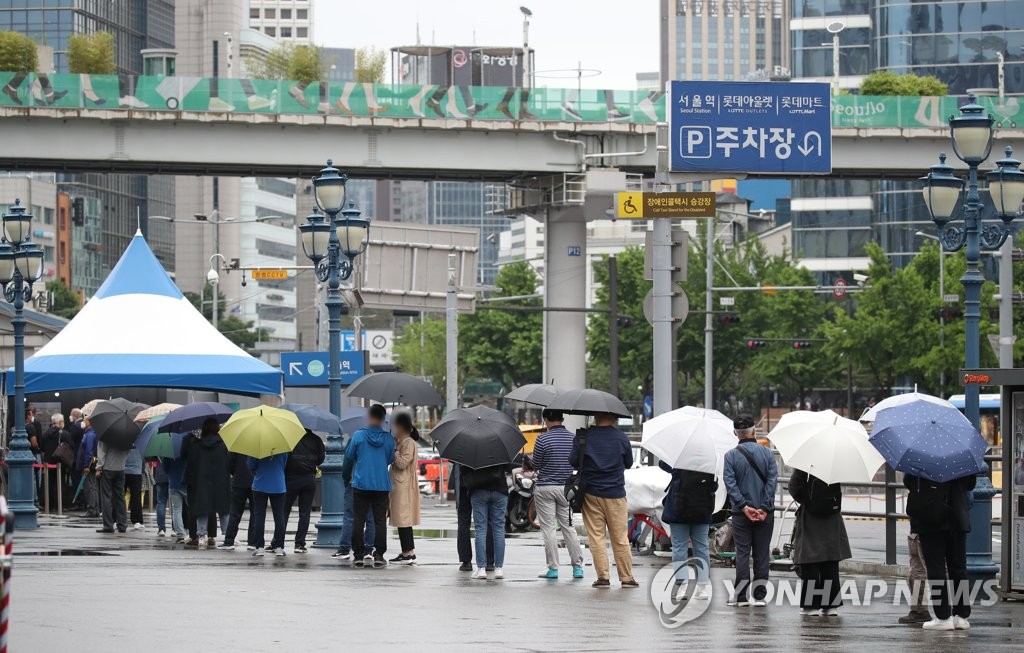 People stand in line in the rain to take coronavirus tests at a makeshift clinic in front of Seoul Station on May 21, 2021. (Yonhap)