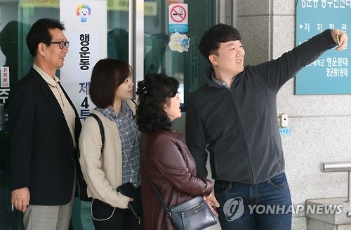 In this file photo, taken on April 13, 2016, a man and his family take a photo in front of a polling booth where they cast their votes in the National Assembly election. Taking photos and sharing them with others to prove or confirm their participation in an election has become sort of a trend among South Koreans, especially the young. (Yonhap)