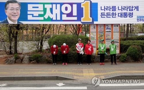 Election campaigners of at least two different presidential candidates, distinguished by the different colors of their jackets, stage a street campaign in Goyang, Gyeonggi Province, on April 17, 2017, while a large street banner of Moon Jae-in, the presidential candidate of the liberal Democratic Party, hangs over their heads. (Yonhap)