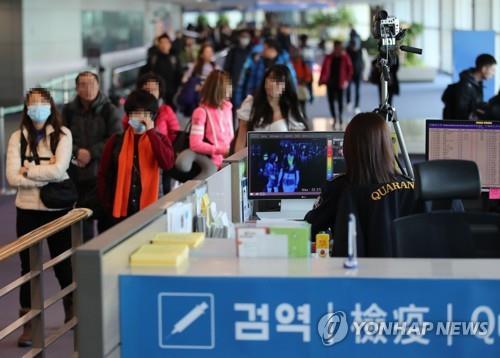 A quarantine official (R) checks passengers arriving at South Korea's Incheon International Airport for signs of fever and other symptoms in this file photo taken on Jan. 9, 2020. (Yonhap)