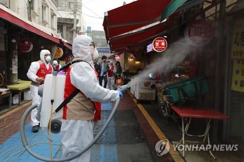 Lotte Group employees in protective suits disinfect a traditional market in Songpa Ward in southeastern Seoul on Feb. 14, 2020, in this photo provided by the retail and trading giant. Many small-time merchants have raised concerns that COVID-19 fear is seriously hurting their businesses as fewer people leave their homes to shop. (PHOTO NOT FOR SALE) (Yonhap)
