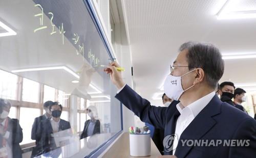 President Moon Jae-in writes a message encouraging students to overcome the coronavirus pandemic together on a glass pane during a visit to a classroom at Jungkyung High School in Seoul on May 8, 2020, to check preparations to begin in-person classes that have been delayed due to the coronavirus crisis. (Yonhap)