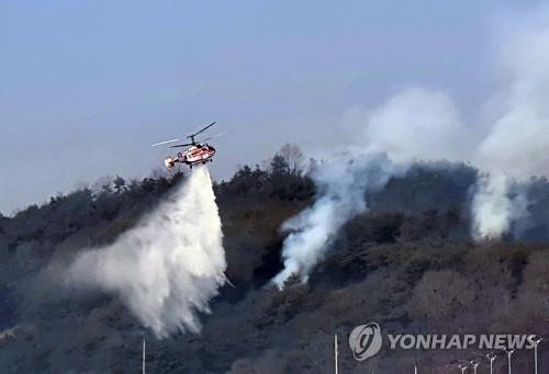 A helicopter drops water over trees to put out flames in Andong, North Gyeongsang Province, on Feb, 22, 2021. (Yonhap)