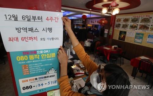 An employee attaches a notice to the entrance of a Chinese restaurant in Seoul on Dec. 3, 2021, that says customers are required to show proof of vaccination or a negative test for entry and that gatherings are capped at six people starting Dec. 6. South Korea said it will limit private gatherings to six people in the capital area and eight in other regions for four weeks, reversing an easing of distancing rules adopted under the "living with COVID-19" scheme last month. (Yonhap)