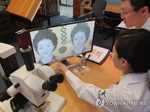 This undated file photo shows bank officials examining a magnified image of what appears to a fake banknote at a Seoul bank. (PHOTO NOT FOR SALE) (Yonhap)