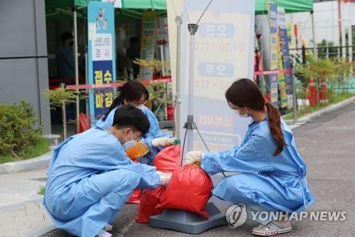 Medical workers put sand bags on standing signboards in preparation for heavy rain and strong winds at a makeshift COVID-19 testing station in the southwestern city of Gwangju on July 13, 2022. (Yonhap)
