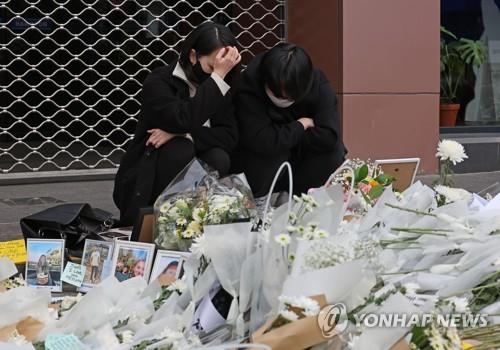 Two people crouch near the site of the deadly Halloween crowd crush, where a sea of flowers and condolence gifts have been laid by mourning citizens, on Nov. 3, 2022. (Yonhap)