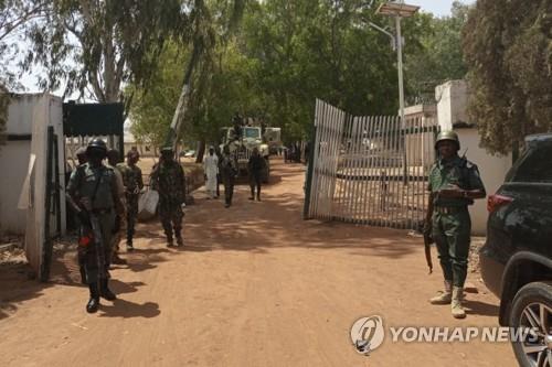 지난 12일 나이지리아 군경이 대학생 집단 납치가 일어난 대학 정문에 서 있다.