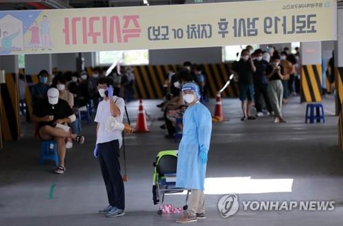 Los trabajadores sanitarios se preparan para trabajar, el 28 de agosto de 2020, mientras que los ciudadanos esperan en línea en una clínica de pruebas de COVID-19 en Gwangju.