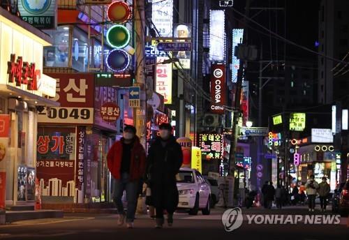 Unos ciudadanos pasan por una avenida llena de tiendas minoristas en el sudeste de Seúl, el 15 de febrero de 2021, el primer día del alivio de las normas de distanciamiento social para los restaurantes y cafeterías.