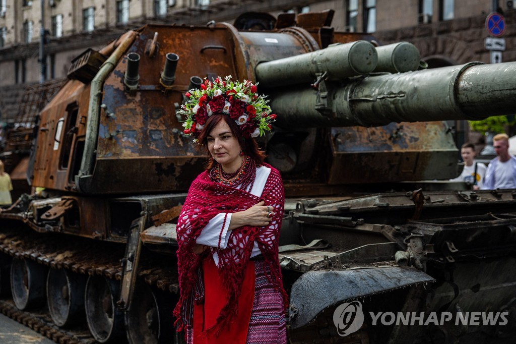 20일 한 여성이 우크라이나 전통 의상을 입고 흐레샤티크 거리에 전시된 러시아군 군용 차량 앞에 서 있다.