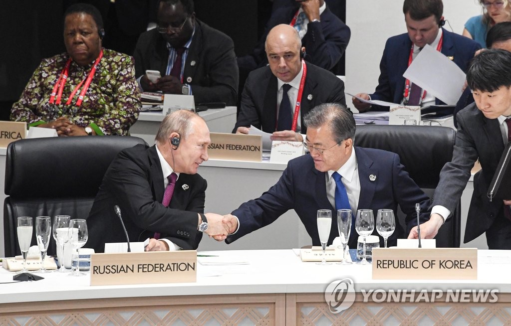 South Korean President Moon Jae-in (R) shakes hands with Russian President Vladimir Putin during a Group of 20 summit session in Osaka, Japan, on June 28, 2019. (Yonhap)