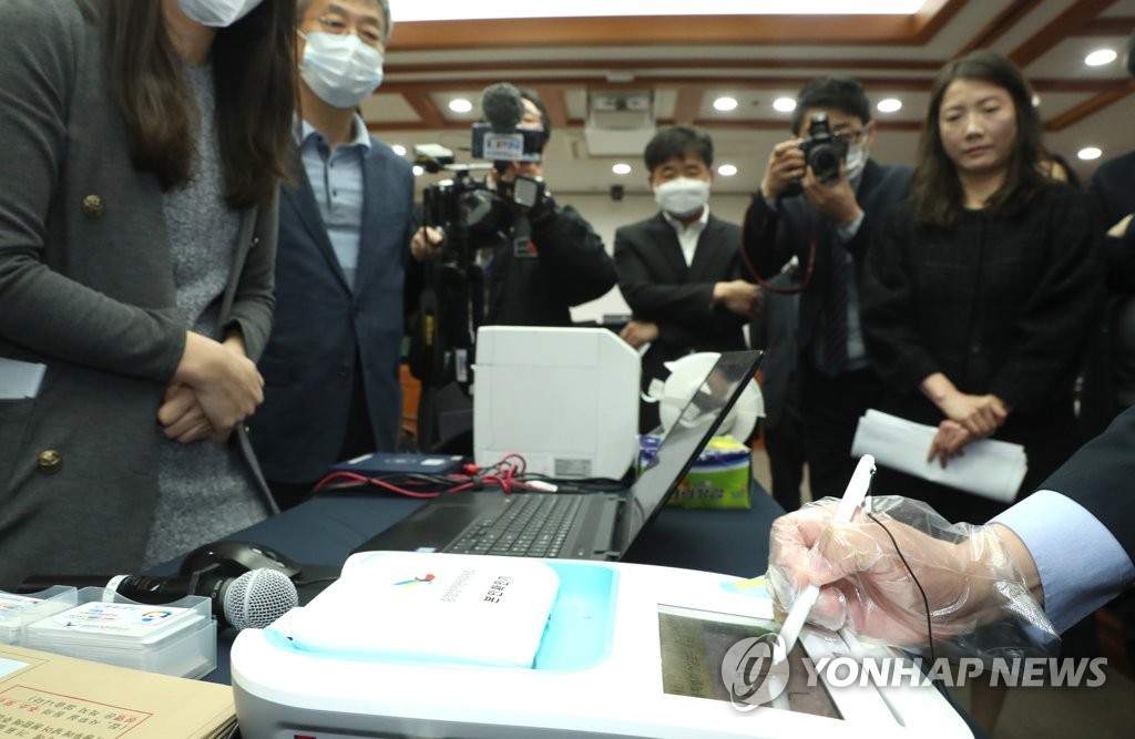 Wearing a plastic glove, an official of the National Election Commission, demonstrates how to cast a ballot for early voting amid the nationwide coronavirus outbreak at the commission's headquarters in Gwacheon, south of Seoul, on March 17, 2020. (Yonhap)