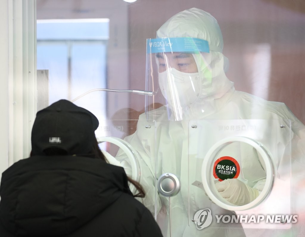 A medical worker collects a specimen from a woman at a temporary COVID-19 screening station in front of Seoul Station on Jan. 3, 2021. (Yonhap)