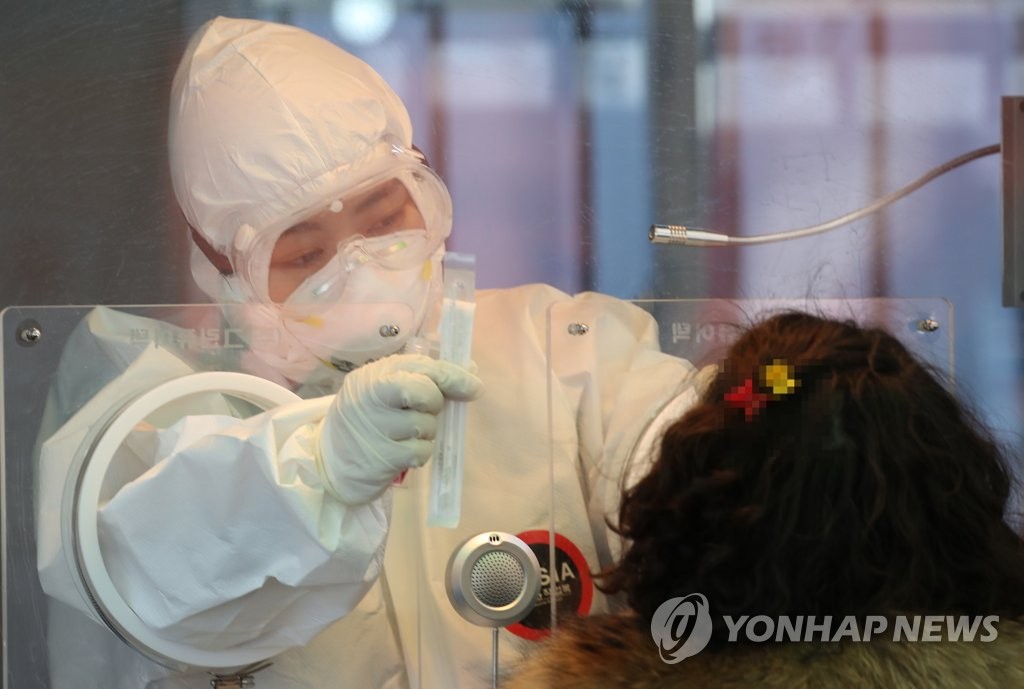A medical worker collects a specimen from a woman in a temporary COVID-19 screening station in front of Seoul Station on Jan. 5, 2021. (Yonhap)