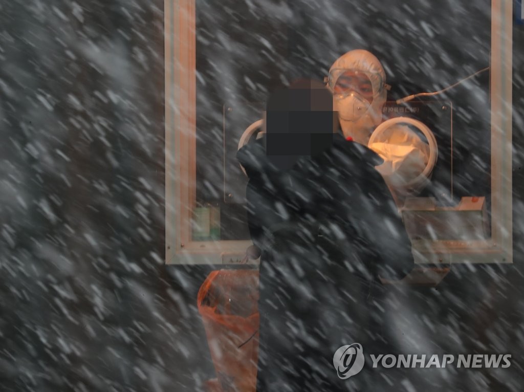 A health worker collects a sample from a citizen at a makeshift COVID-19 testing facility amid snowfall in Seoul on Jan. 18, 2021. (Yonhap)
