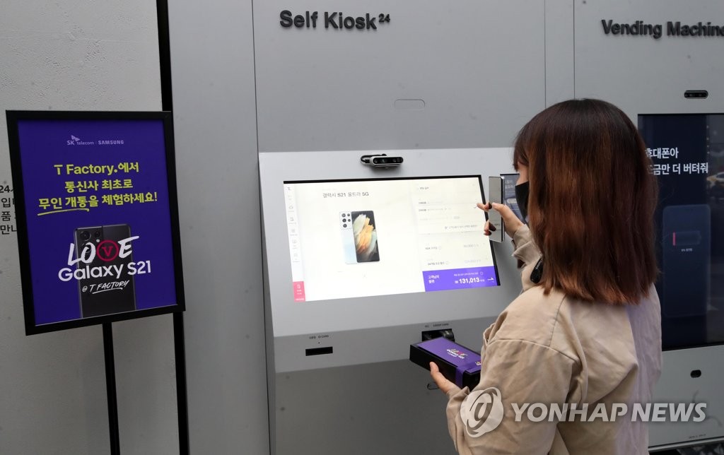 This file photo, taken Jan. 22, 2021, shows a customer at SK Telecom Co.'s store in western Seoul receiving Samsung Electronics Co.'s Galaxy S21 smartphone from a digital kiosk. (Yonhap)