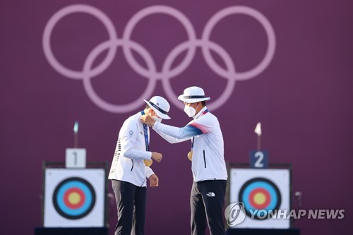 South Korean archer Kim Je-deok (R) puts the gold medal around the neck of his teammate An San during the medal ceremony for the mixed team event at the Tokyo Olympics at Yumenoshima Park Archery Field in Tokyo on July 24, 2021. (Yonhap)