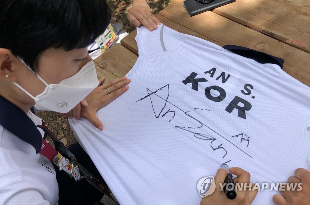 South Korean archer An San signs his uniform at Yumenoshima Park Archery Field in Tokyo on July 31, 2021, before donating it to the International Olympic Committee's Olympic Museum in Switzerland, in the photo provided by the Korea Archery Association on Aug. 1. (PHOTO NOT FOR SALE) (Yonhap)