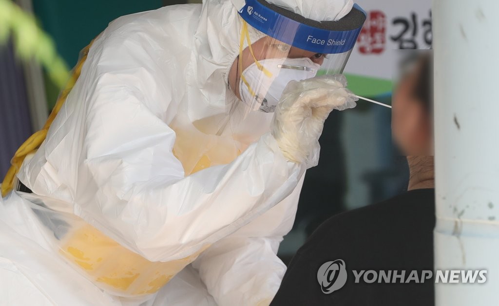 A health worker in a protective suit collects a sample from a citizen at a virus testing clinic in Gimhae, South Gyeongsang Province, on Aug. 4, 2021. (Yonhap)