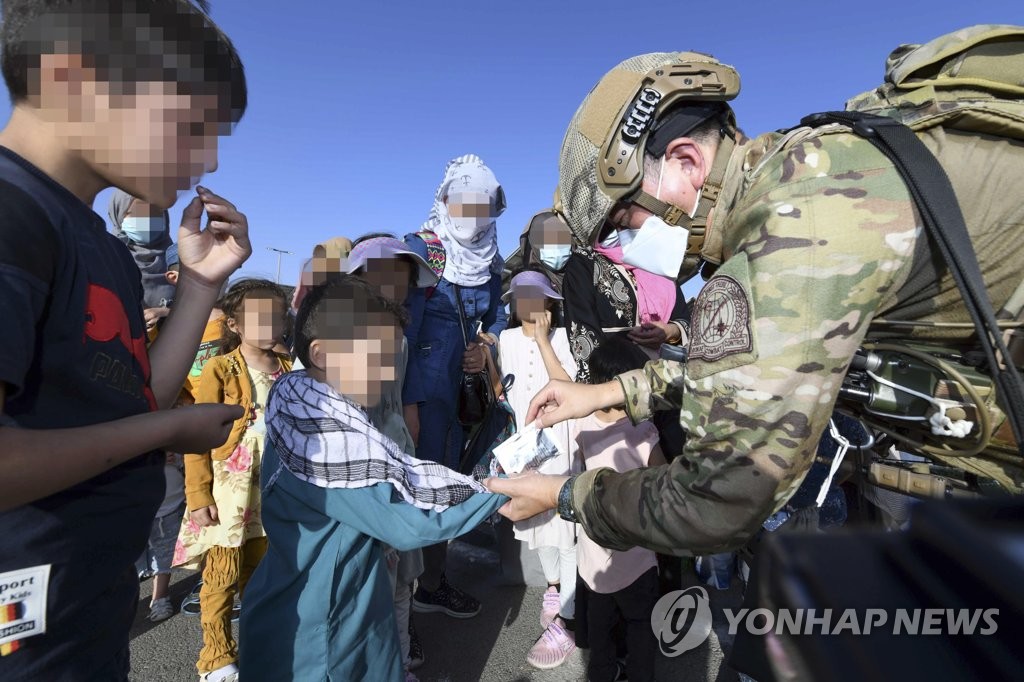 A South Korean soldier of an Air Force's special forces unit gives out snacks to Afghan children, before they and their parents are flown out of Kabul on a military plane in an evacuation operation to bring a total of 391 Afghans who worked for the South and their families to Seoul, in this photo provided by the Air Force on Aug. 26, 2021. (PHOTO NOT FOR SALE) (Yonhap) 