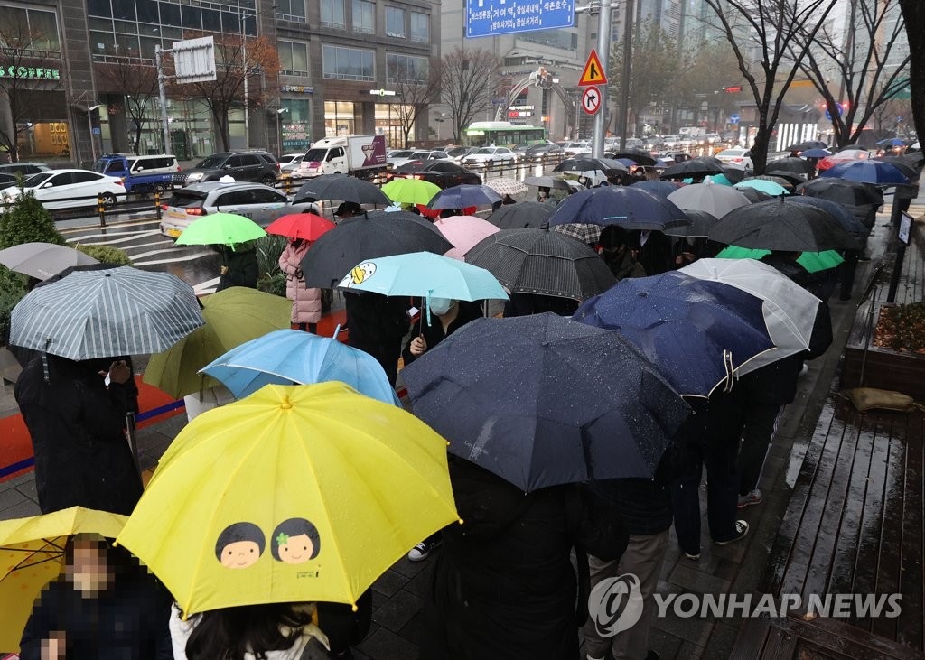 Des citoyens abrités sous leur parapluie font la queue avant de se soumettre à un test de dépistage du nouveau coronavirus (Covid-19), le mardi 30 novembre 2021, devant le centre médical public de Songpa, dans le sud-est de Séoul. 