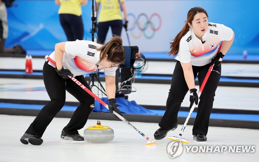 South Korean curlers Kim Seon-yeong (L) and Kim Yeong-mi sweep the ice during the women's curling round-robin match against Japan at the Beijing Winter Olympics at the National Aquatics Centre on Feb. 14, 2022. (Yonhap)