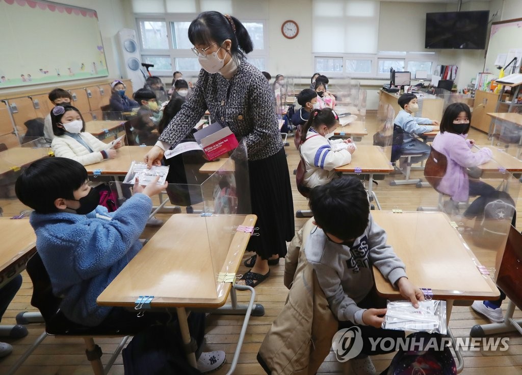 This photo taken on March 2, 2022, shows a teacher handing out COVID-19 self-test kits to students at Bongmu Elementary School in Daegu, 300 kilometers south of Seoul, amid the rapid spread of omicron virus variant. (Yonhap)