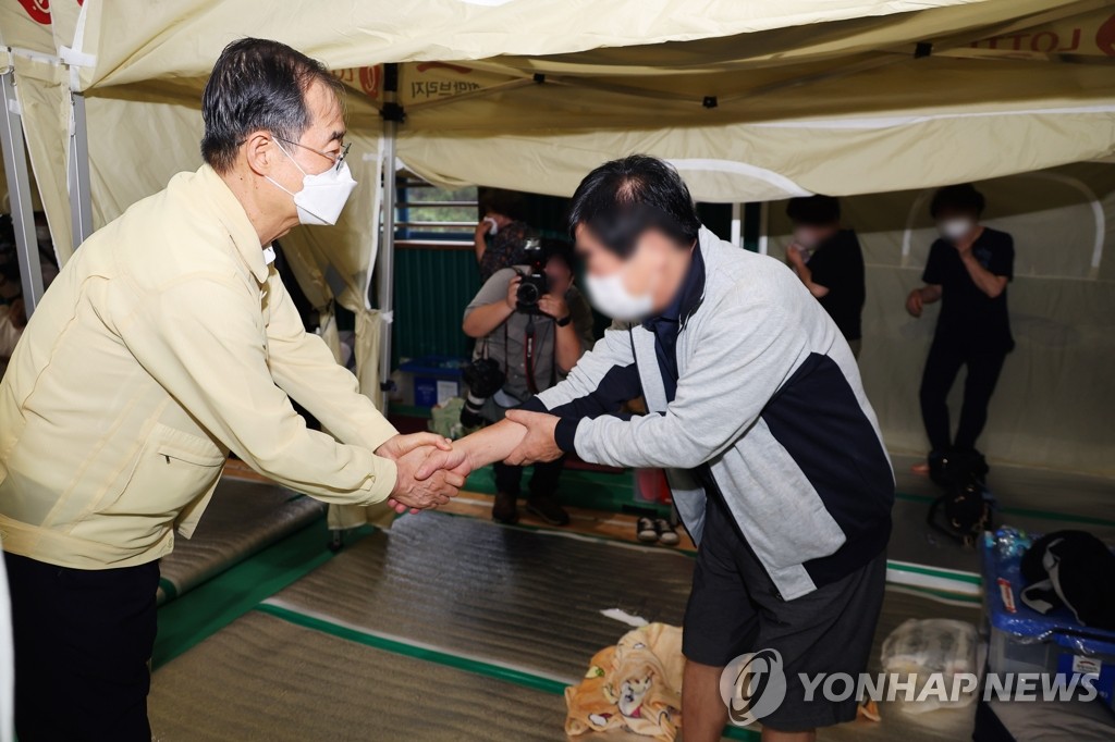 Prime Minister Han Duck-soo shakes hands with a resident from Guryong Village at a temporary shelter in Seoul on Aug. 9, 2022. (Yonhap)