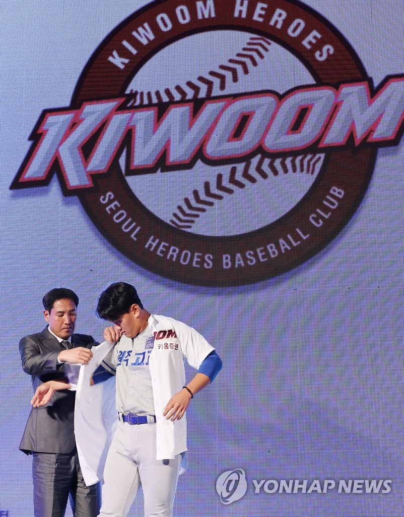 Wonju High School pitcher-catcher Kim Geon-hee (R) dons the Kiwoom Heroes jersey, with the help of the club's general manager, Ko Hyung-wook, during the Korea Baseball Organization draft at Westin Josun Hotel in Seoul on Sept. 15, 2022. (Yonhap)