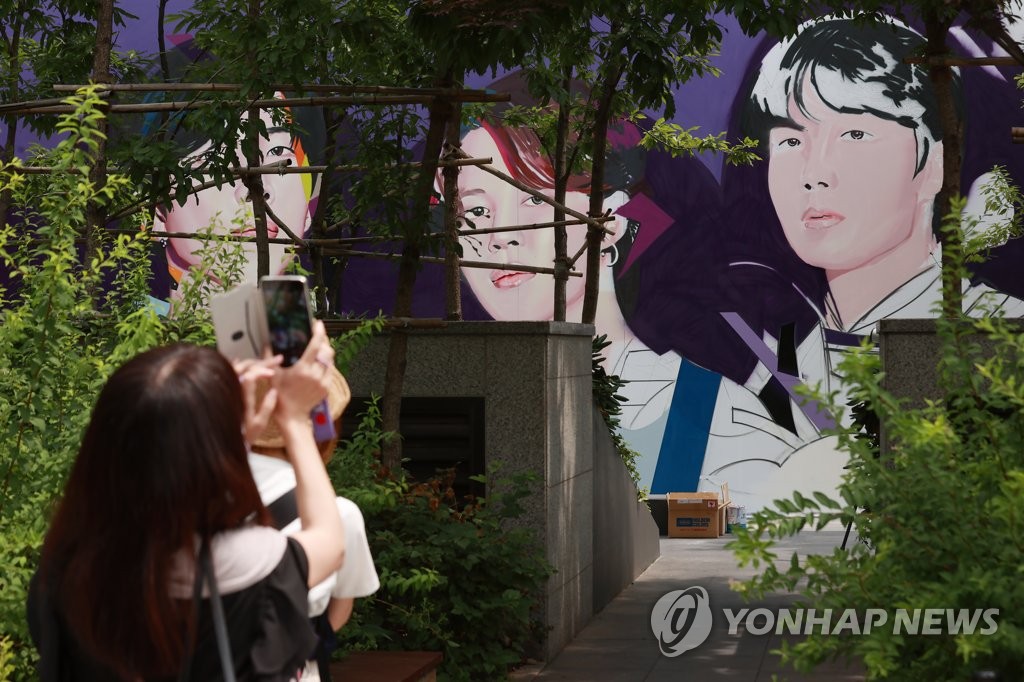 A fan takes a picture of a graffiti drawing of BTS members on the outer wall of K-pop powerhouse Hybe's office building in central Seoul. (Yonhap)