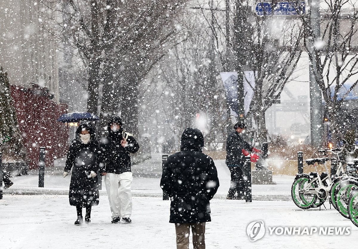 La gente camina por una calle cerca del Palacio Deoksu, en el centro de Seúl, en medio de fuertes nevadas, el 30 de diciembre de 2023. La agencia meteorológica estatal emitió un aviso de fuertes nevadas para partes de la capital y sus alrededores.  (Yonhap)