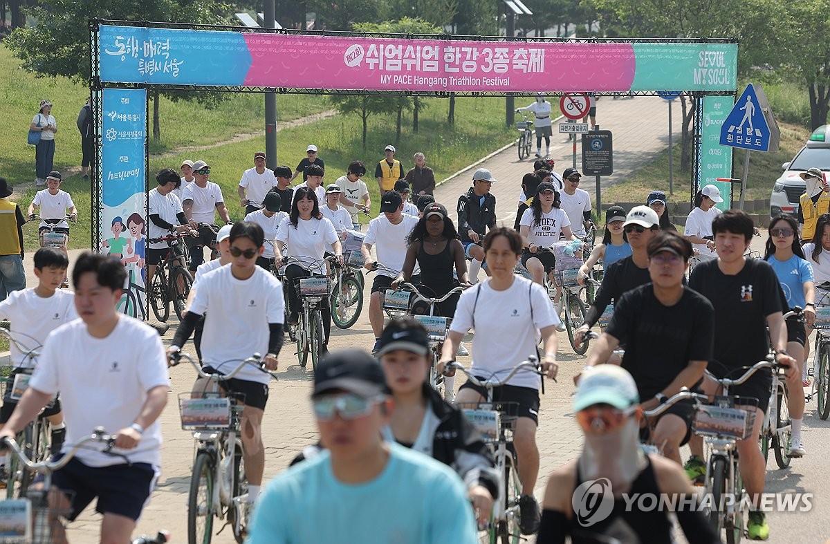 Han River Triathlon Festival participants cycling along the river with Seoul's skyline in the background